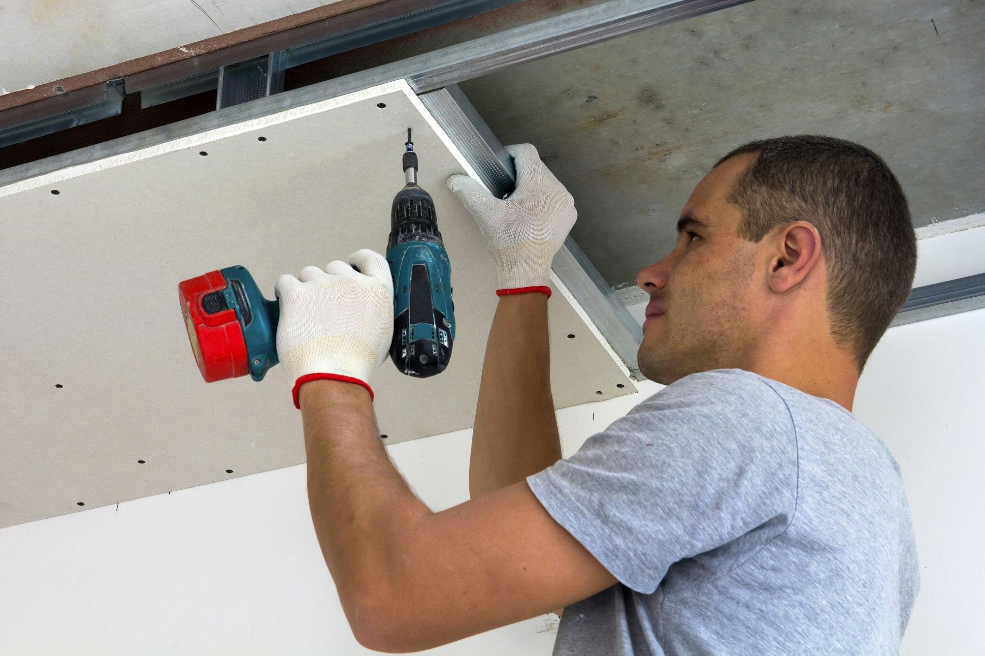 Construction worker assemble a suspended ceiling with drywall and fixing the drywall to the ceiling